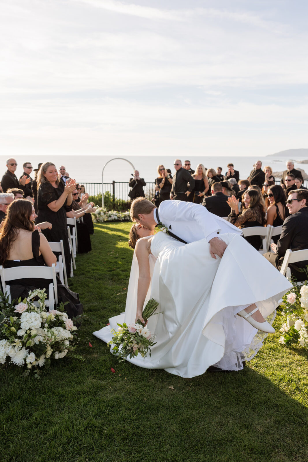 Newlyweds sharing a romantic dip kiss at the end of the aisle after their cliffside ceremony in Pismo Beach, California, captured by Southern California wedding photographer