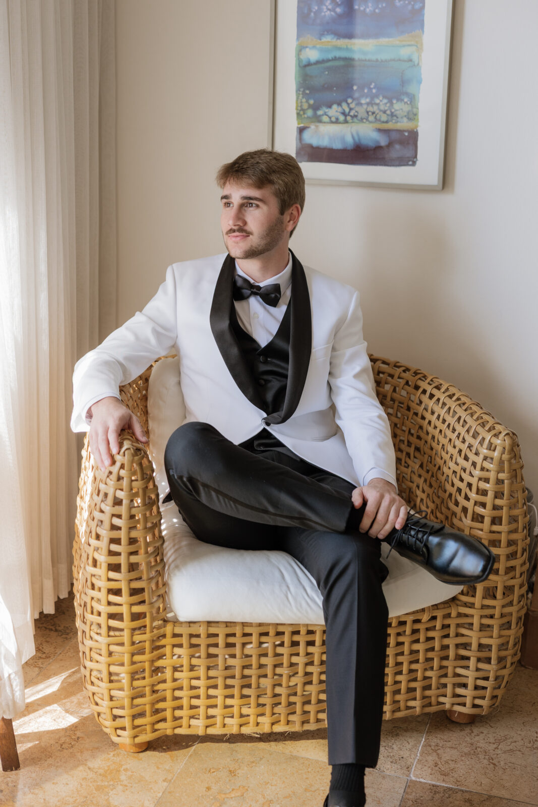 Groom sitting down while getting ready on wedding day in Pismo Beach, California, candid moment captured by Southern California wedding photographer