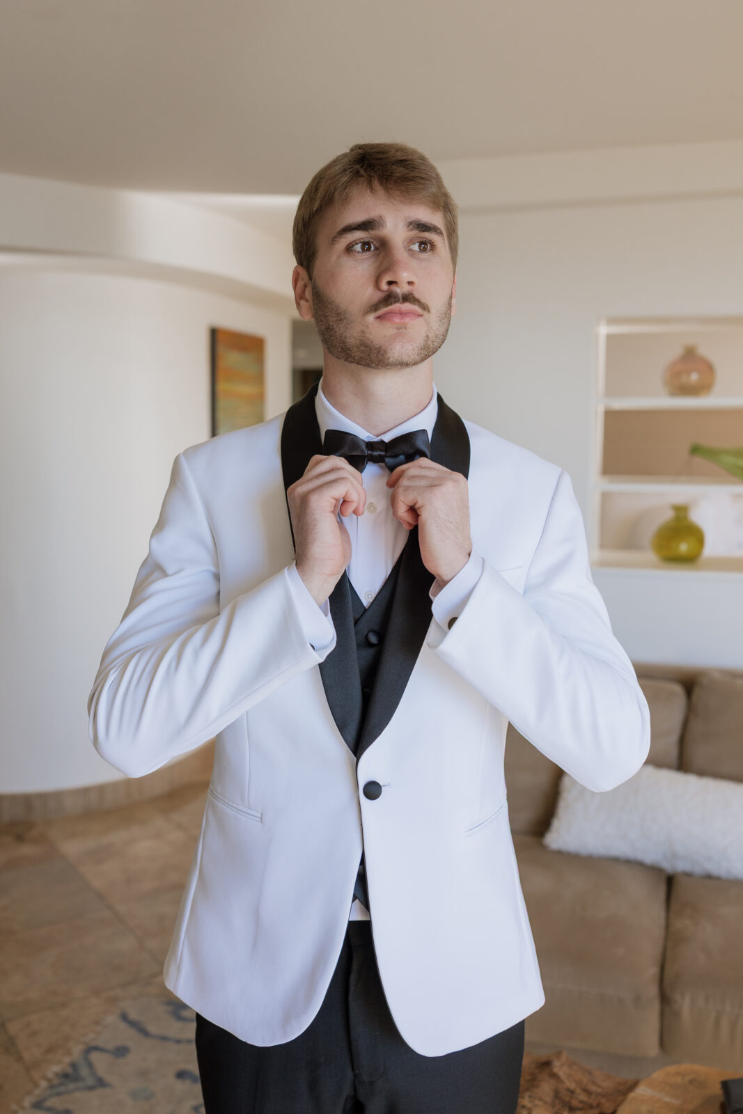 Groom standing and adjusting his tie while getting ready for cliffside wedding in Pismo Beach, California, captured by Southern California wedding photographer