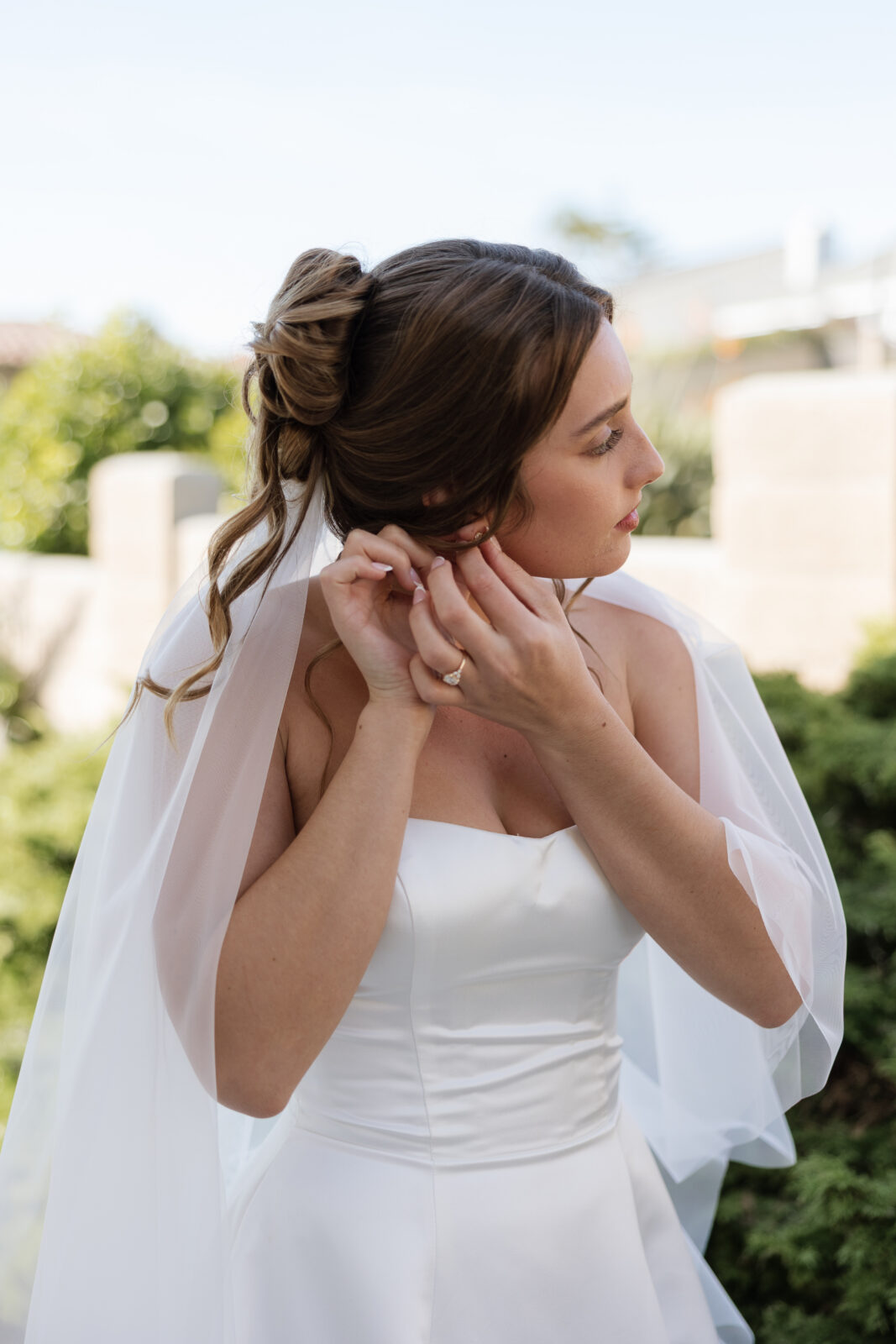 Bride putting on earrings while getting ready on wedding day in Pismo Beach, California, soft natural light captured by Southern California wedding photographer