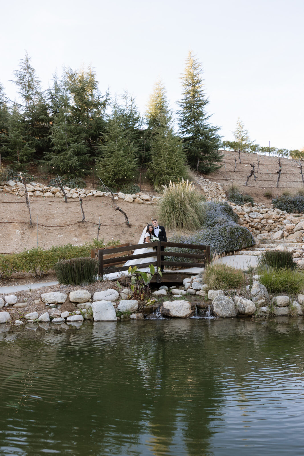 Chelsea and Blake posing by a pond at Serendipity Garden in Oak Glen, California, romantic outdoor wedding portrait