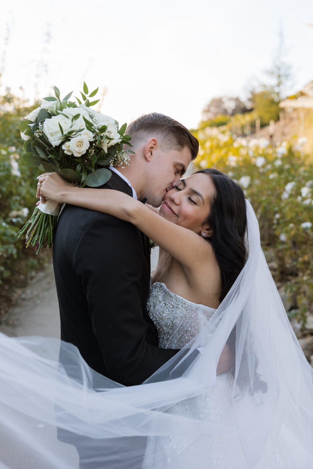 Bride and groom Chelsea and Blake wrapped in her veil during sunset portraits at Serendipity Garden in Oak Glen, California